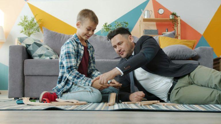 Dad businessman is playing with adorable little son holding toys relaxing in leisure time in house. Business people, family life and indoor activities concept.